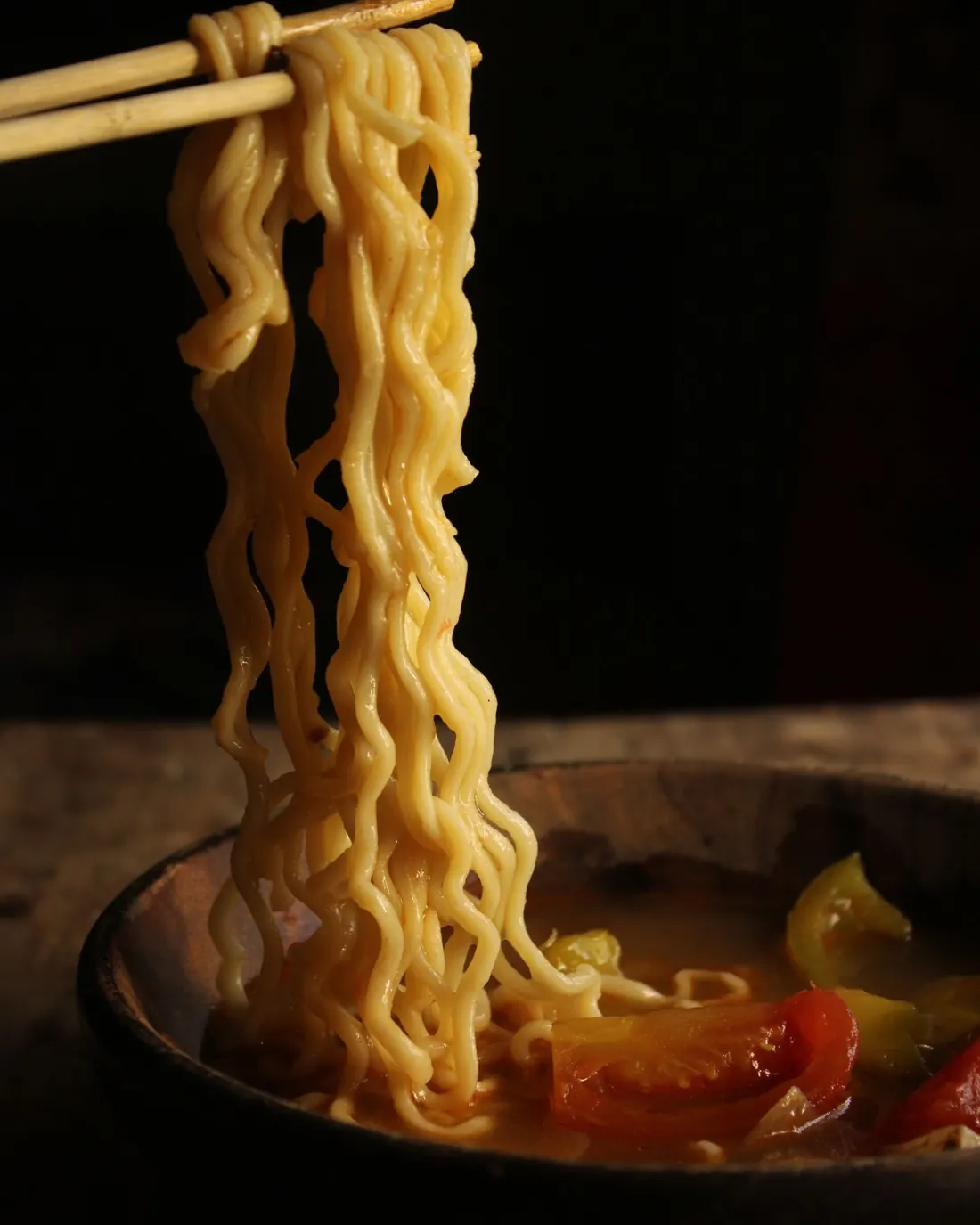 Nouilles ramen soulevées avec des baguettes au-dessus d’un bol fumant